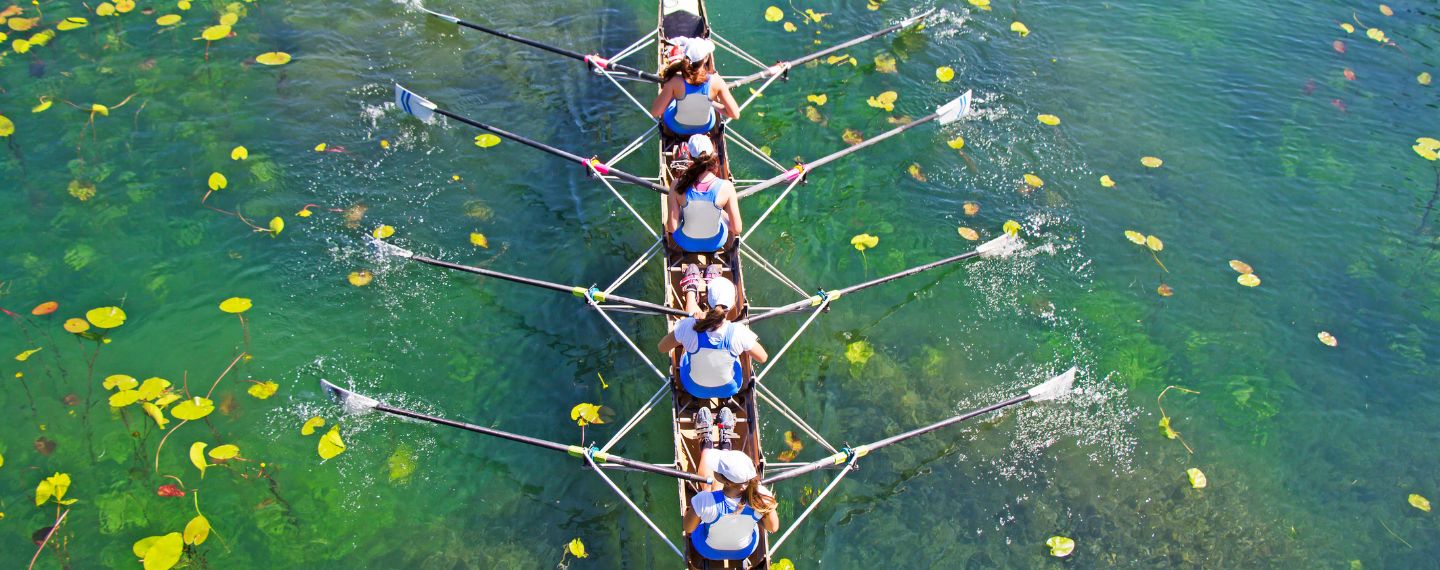 Vier Frauen rudern im selben Takt auf einem See